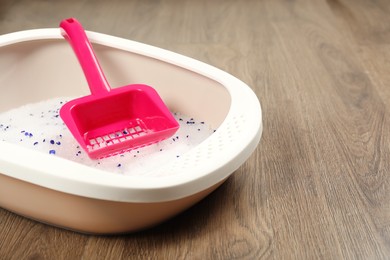 Cat litter tray with filler and scoop on wooden floor, closeup