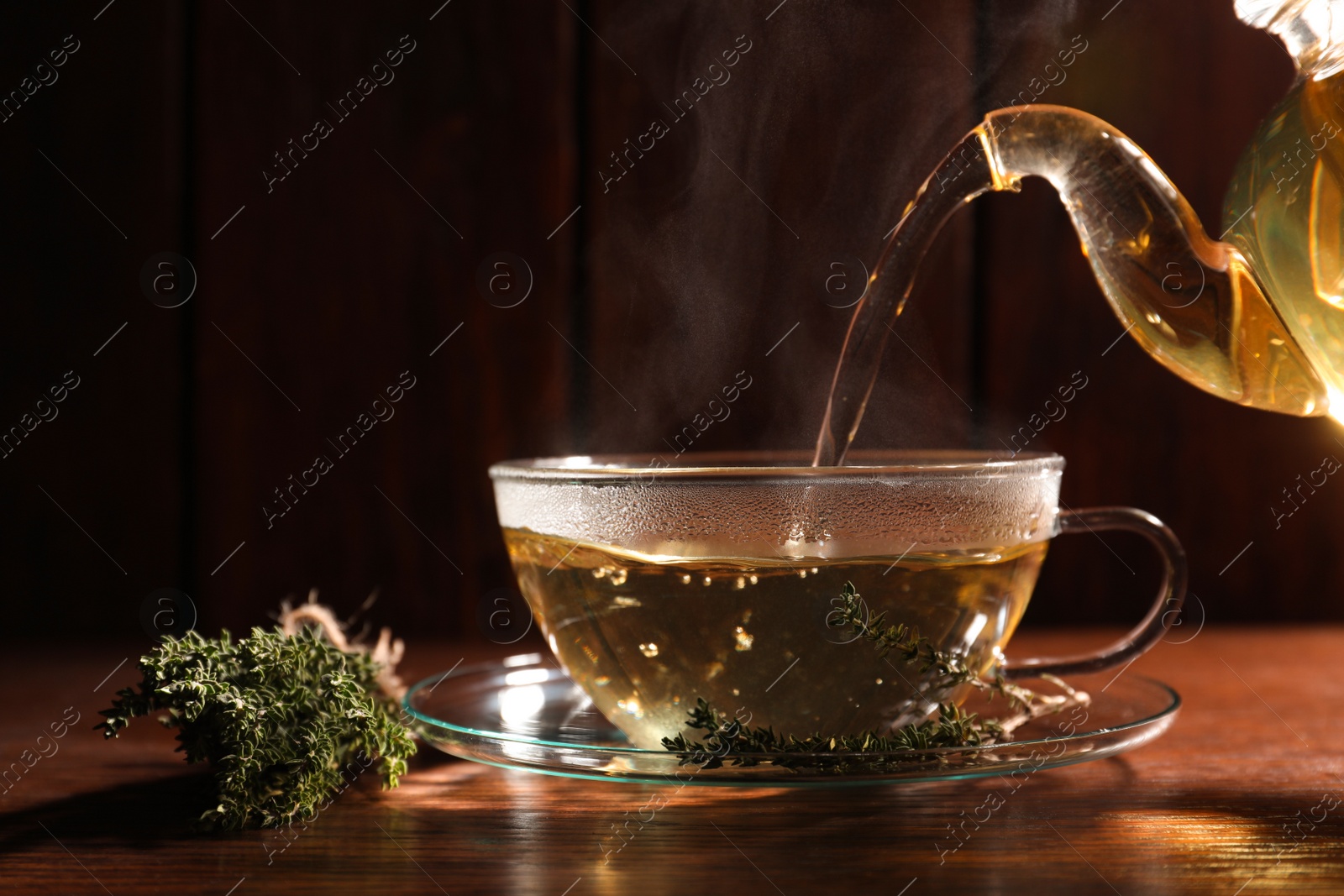 Photo of Pouring aromatic herbal tea into cup and thyme on wooden table