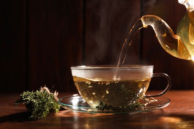 Pouring aromatic herbal tea into cup and thyme on wooden table