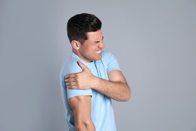 Man suffering from shoulder pain on grey background