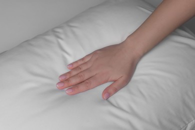 Photo of Woman touching soft white pillow on bed, closeup