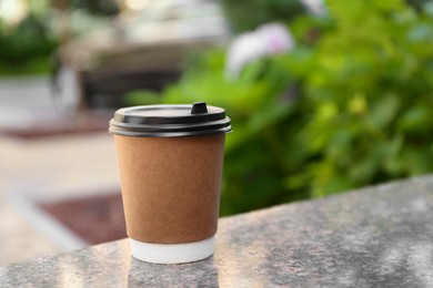 Paper cup with hot coffee on table outdoors, space for text. Takeaway drink
