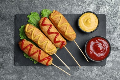 Photo of Delicious deep fried corn dogs with lettuce and sauces on grey table, top view