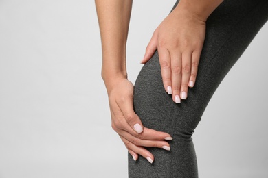 Woman having knee problems on grey background, closeup
