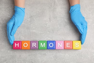 Doctor making word HORMONES with colorful cubes at grey table, top view