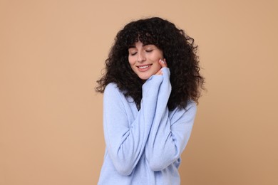 Happy young woman in stylish light blue sweater on beige background