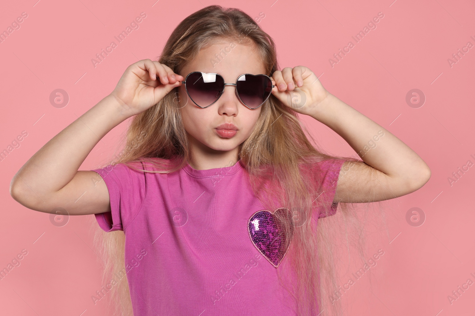 Photo of Girl wearing stylish sunglasses in shape of hearts on pink background