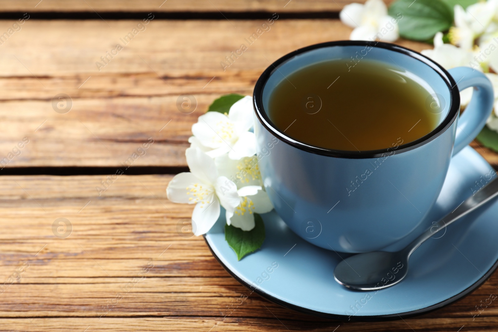 Photo of Cup of tea and fresh jasmine flowers on wooden table. Space for text