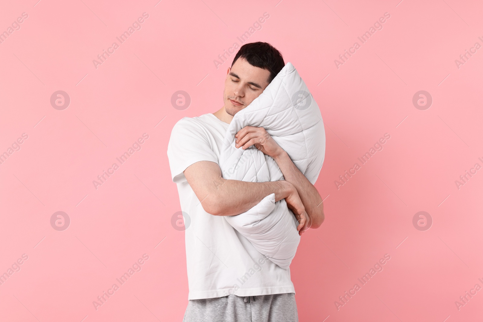 Photo of Man in pyjama holding pillow and sleeping on pink background