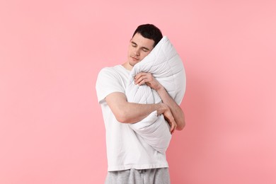 Man in pyjama holding pillow and sleeping on pink background