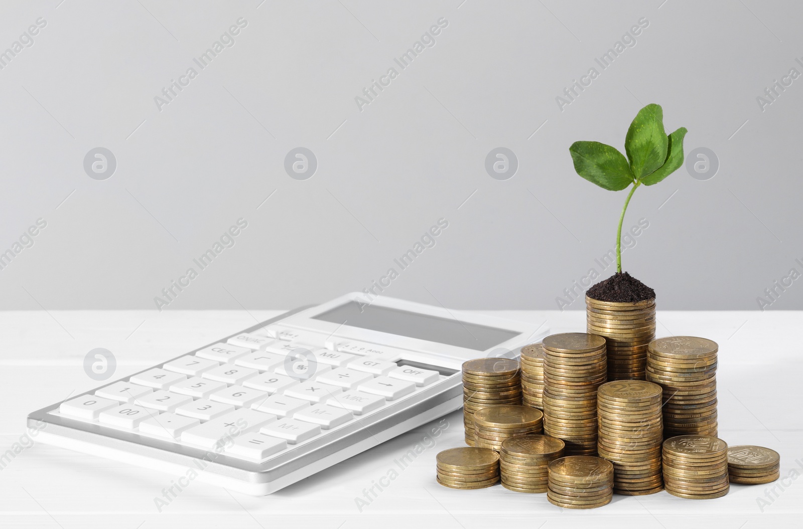 Photo of Stacks of coins with green sprout and calculator on white table, space for text. Investment concept