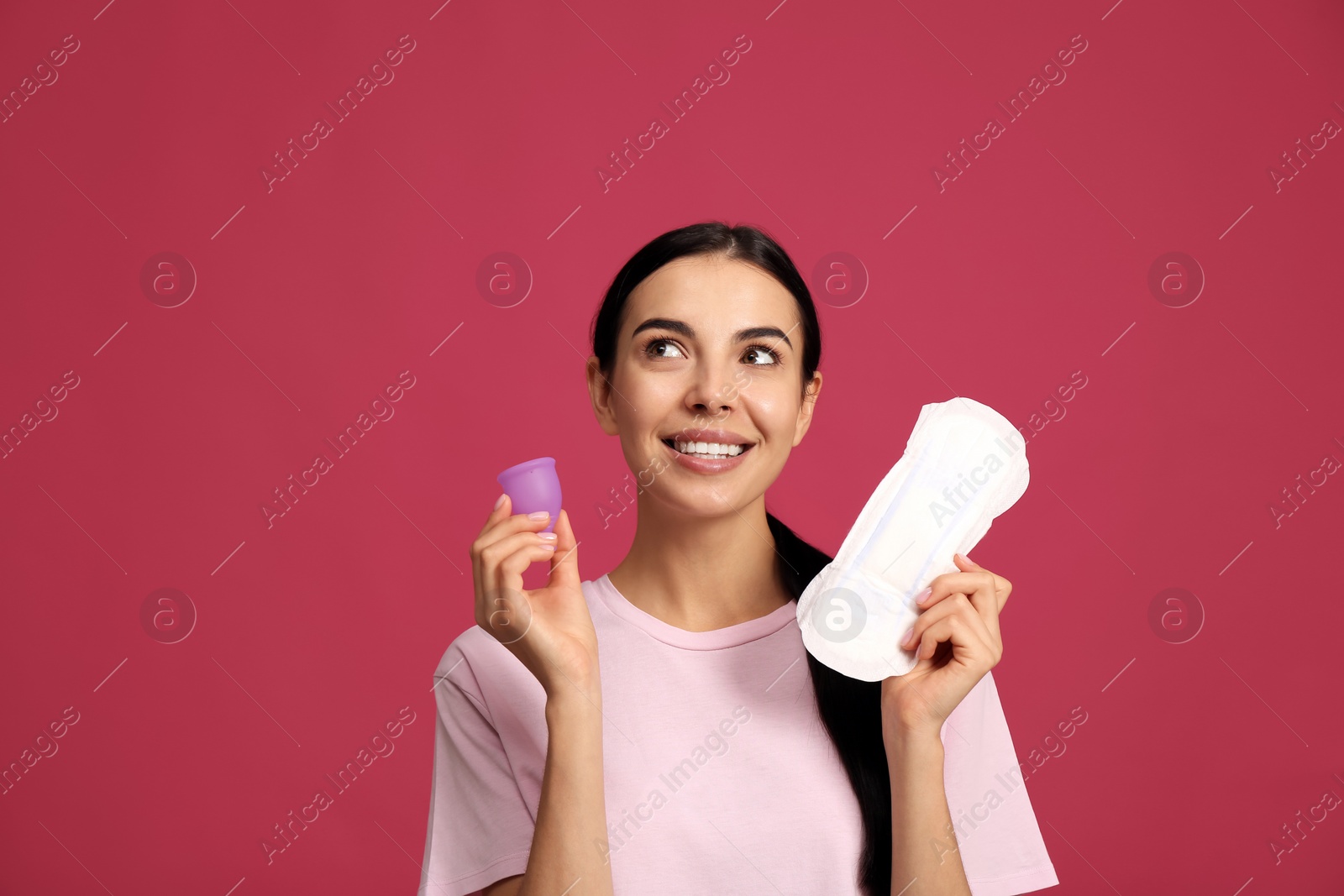 Photo of Young woman with menstrual cup and pad on bright pink background