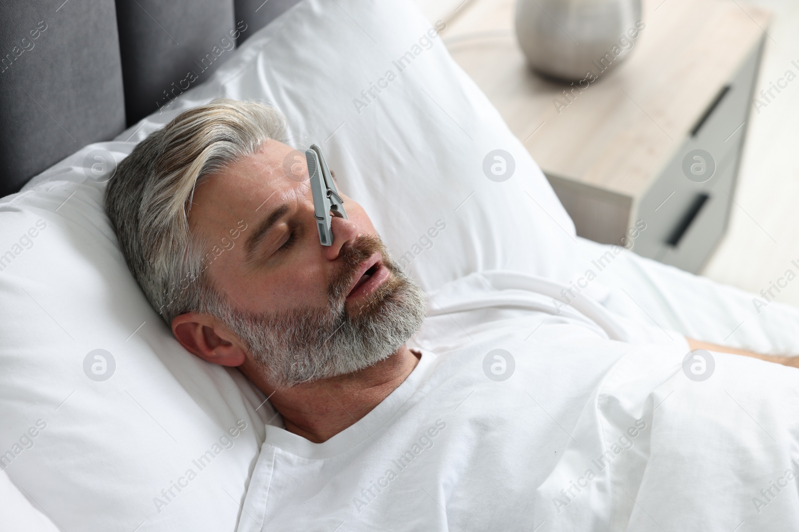 Photo of Man sleeping with clothespin on his nose in bed at home. Problem with snoring