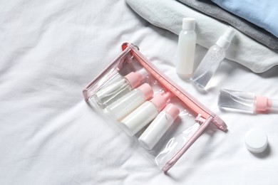 Photo of Cosmetic travel kit. Plastic bag with small containers of personal care products on bed, above view