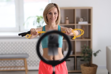 Smiling sports blogger holding skipping rope while streaming online fitness lesson with smartphone at home