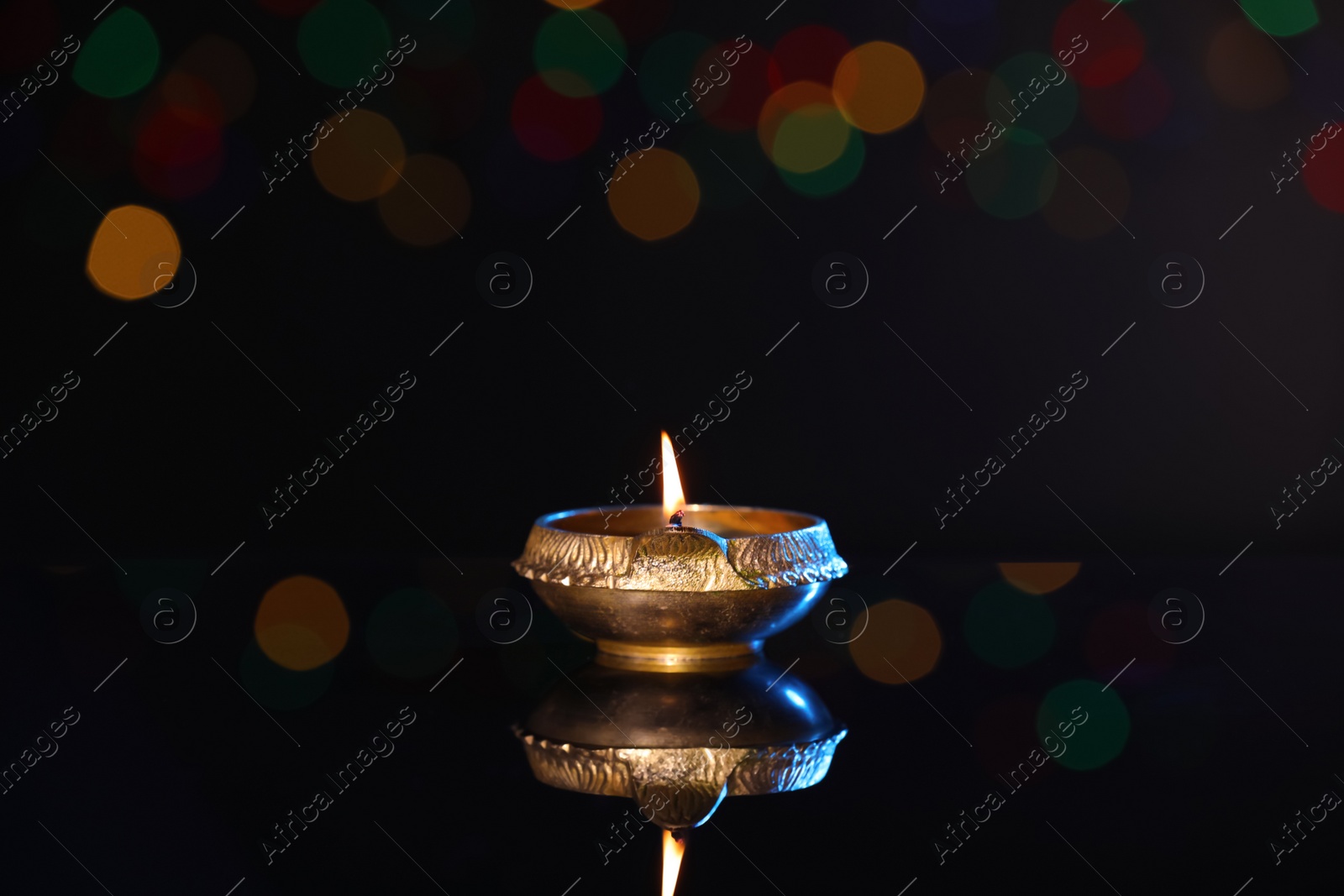 Photo of Lit diya on dark background with blurred lights, space for text. Diwali lamp