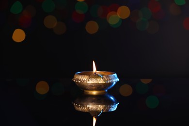 Photo of Lit diya on dark background with blurred lights, space for text. Diwali lamp