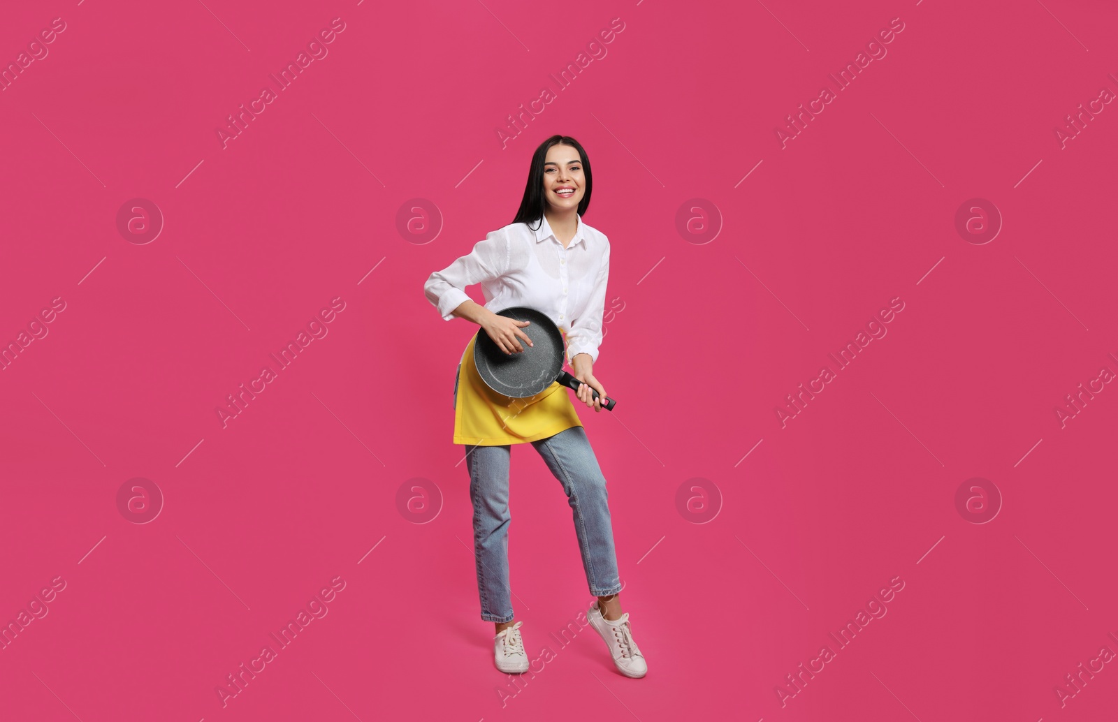 Photo of Young housewife with frying pan having fun on pink background