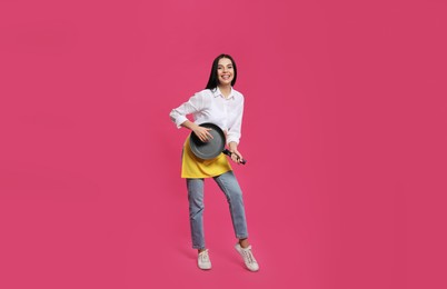 Photo of Young housewife with frying pan having fun on pink background