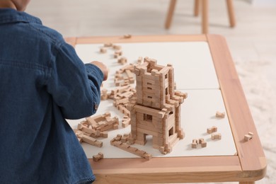 Little boy playing with wooden tower at table indoors, closeup. Child's toy