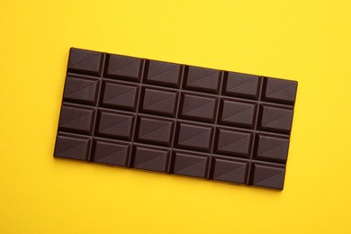 Photo of Tasty chocolate bar on yellow background, top view