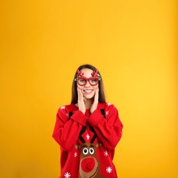 Young woman in Christmas sweater and party glasses on yellow background, space for text