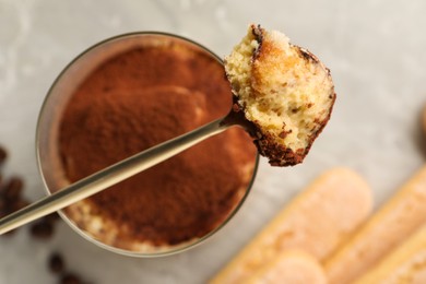 Photo of Tasty tiramisu in glass, spoon and biscuits on light grey table, flat lay