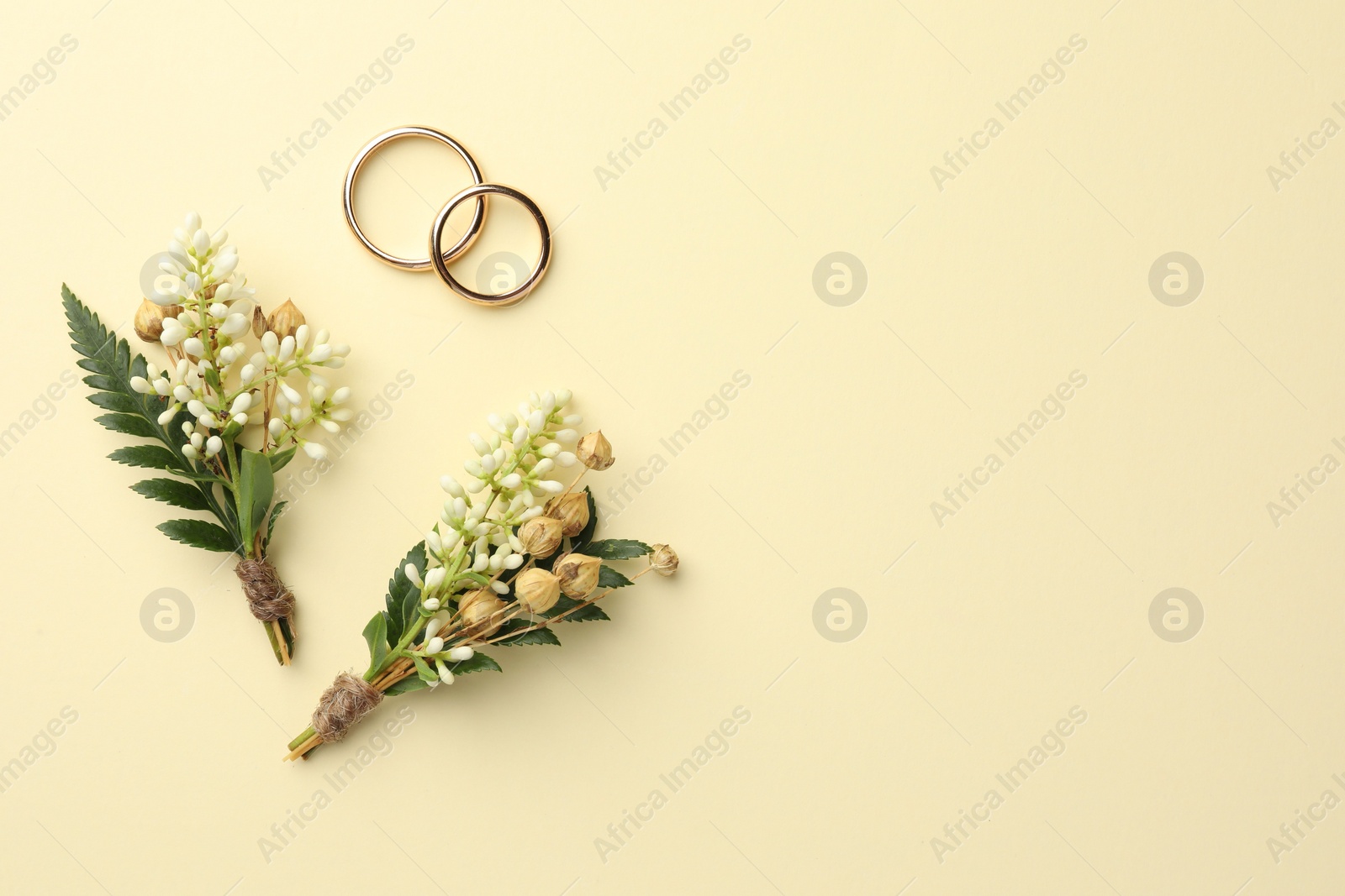 Photo of Small stylish boutonnieres and rings on beige background, flat lay. Space for text