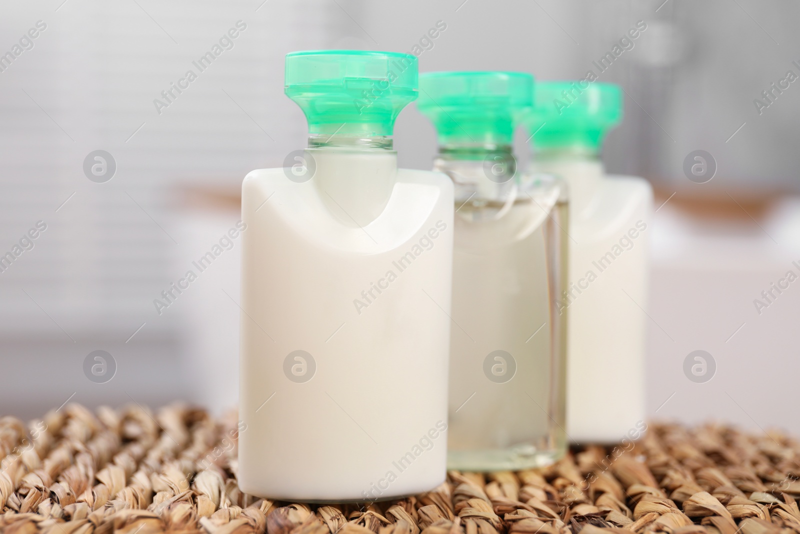 Photo of Mini bottles of cosmetic products on wicker mat against blurred background, closeup