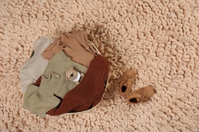 Laundry basket with baby clothes, shoes and crochet toy on beige rug, flat lay