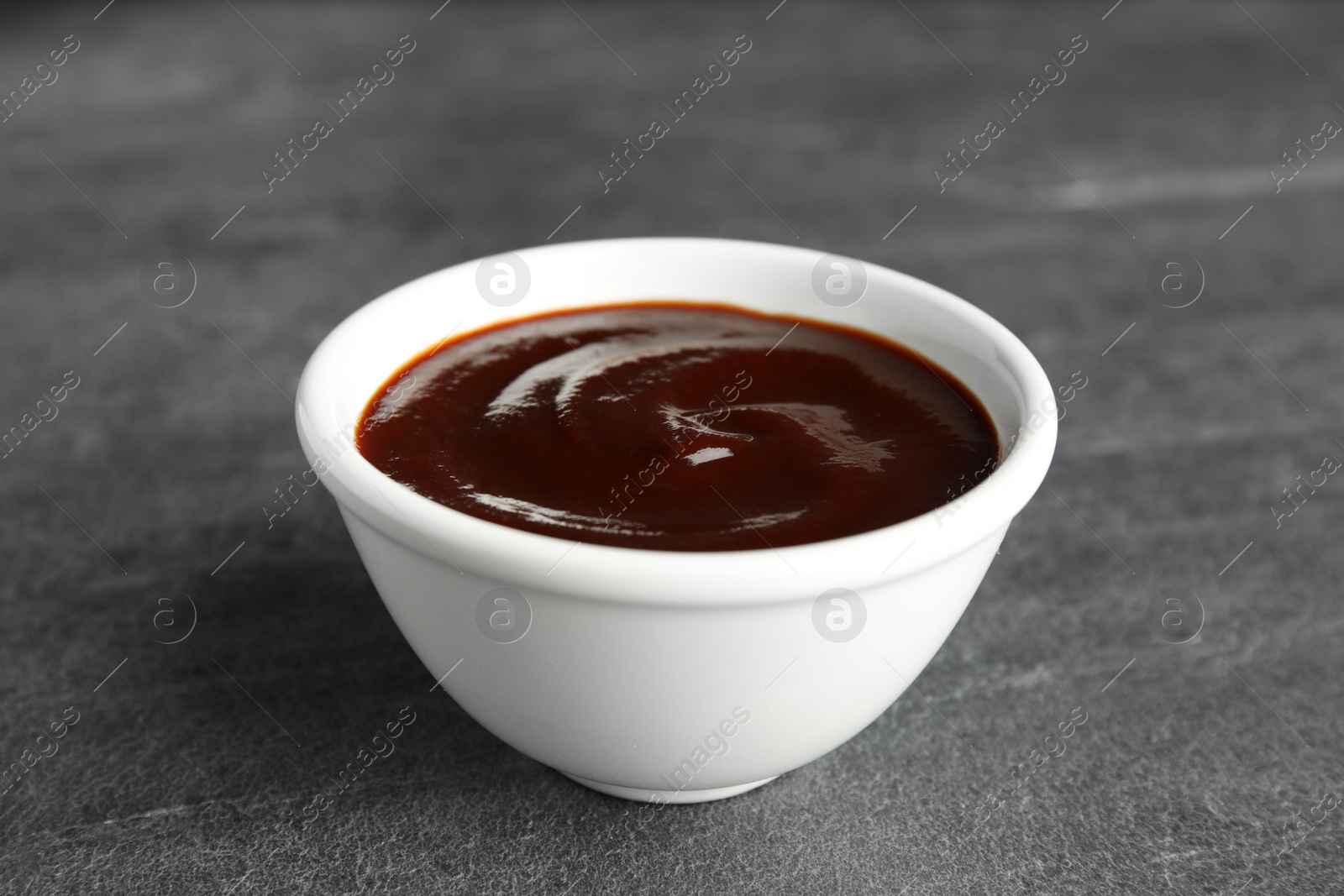 Photo of Barbecue sauce in bowl on grey background