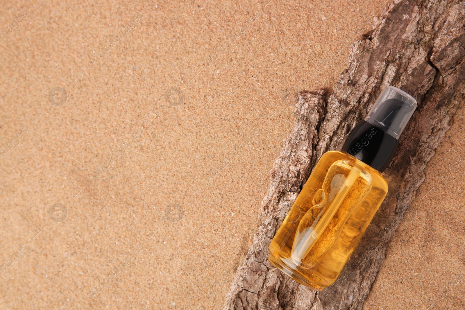 Photo of Bottle of serum and tree bark on sand, top view. Space for text