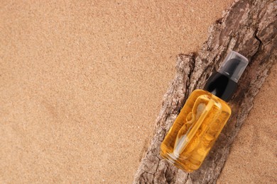 Photo of Bottle of serum and tree bark on sand, top view. Space for text