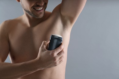 Man applying deodorant on grey background, closeup. Space for text