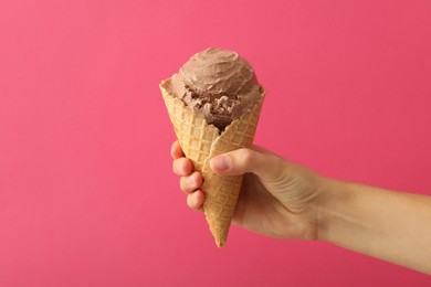 Woman holding waffle cone with delicious chocolate ice cream on pink background, closeup