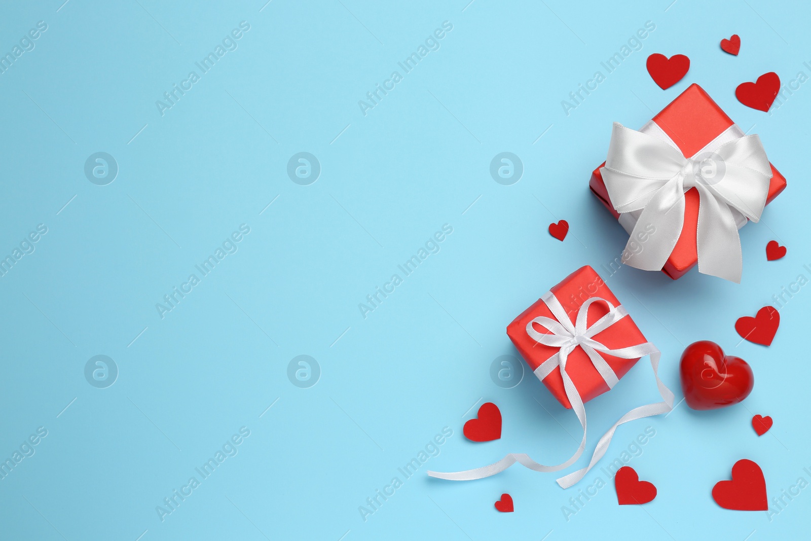 Photo of Beautiful gift boxes and red decorative hearts on light blue background, flat lay. Space for text