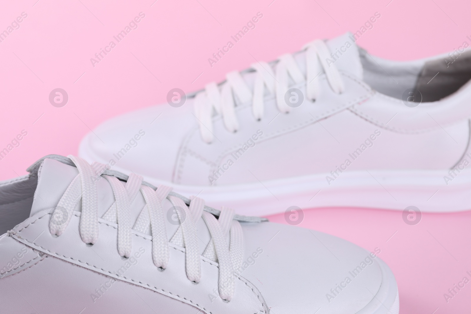 Photo of Pairstylish white sneakers on pink background, closeup