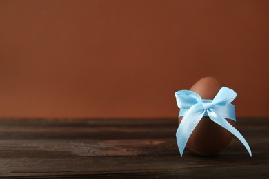 Photo of Tasty chocolate egg with light blue bow on wooden table, space for text