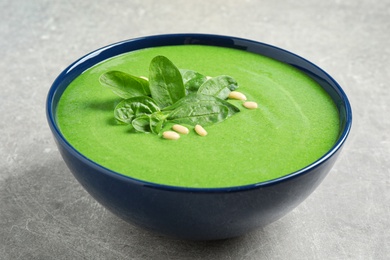 Photo of Bowl of healthy green soup with fresh spinach on grey table