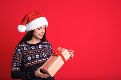 Young beautiful woman in Santa hat with gift box on color background. Christmas celebration