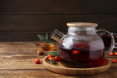 Photo of Teapot with aromatic rose hip tea and fresh berries on wooden table, space for text