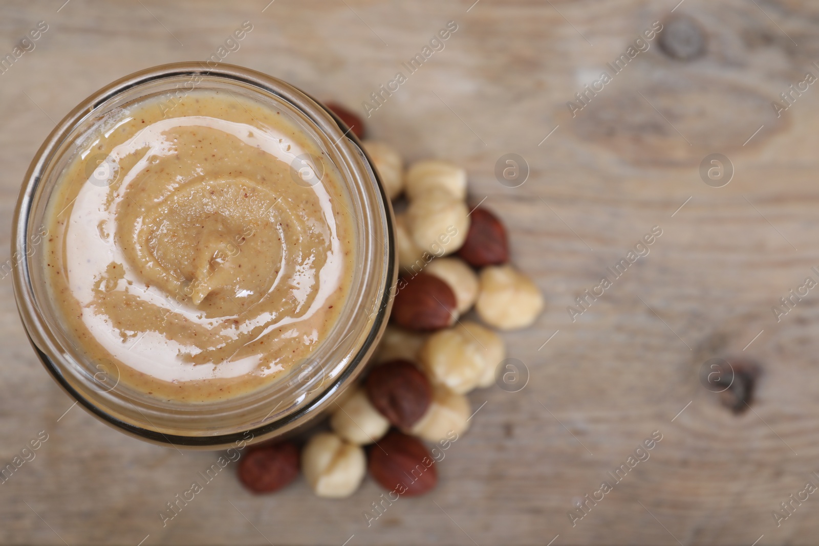 Photo of Tasty hazelnut nut paste in jar on table, top view. Space for text