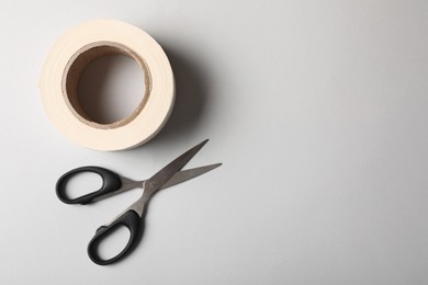 Photo of Roll of adhesive tape and scissors on light background, top view. Space for text