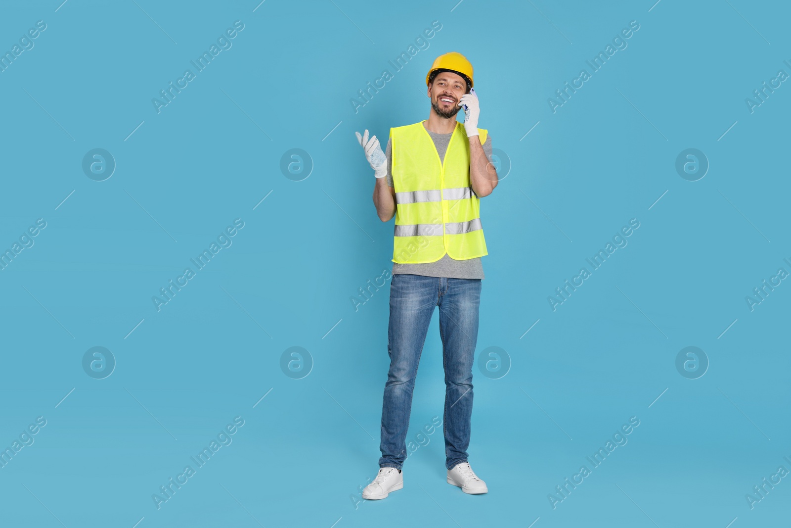 Photo of Male industrial engineer in uniform talking on phone against light blue background