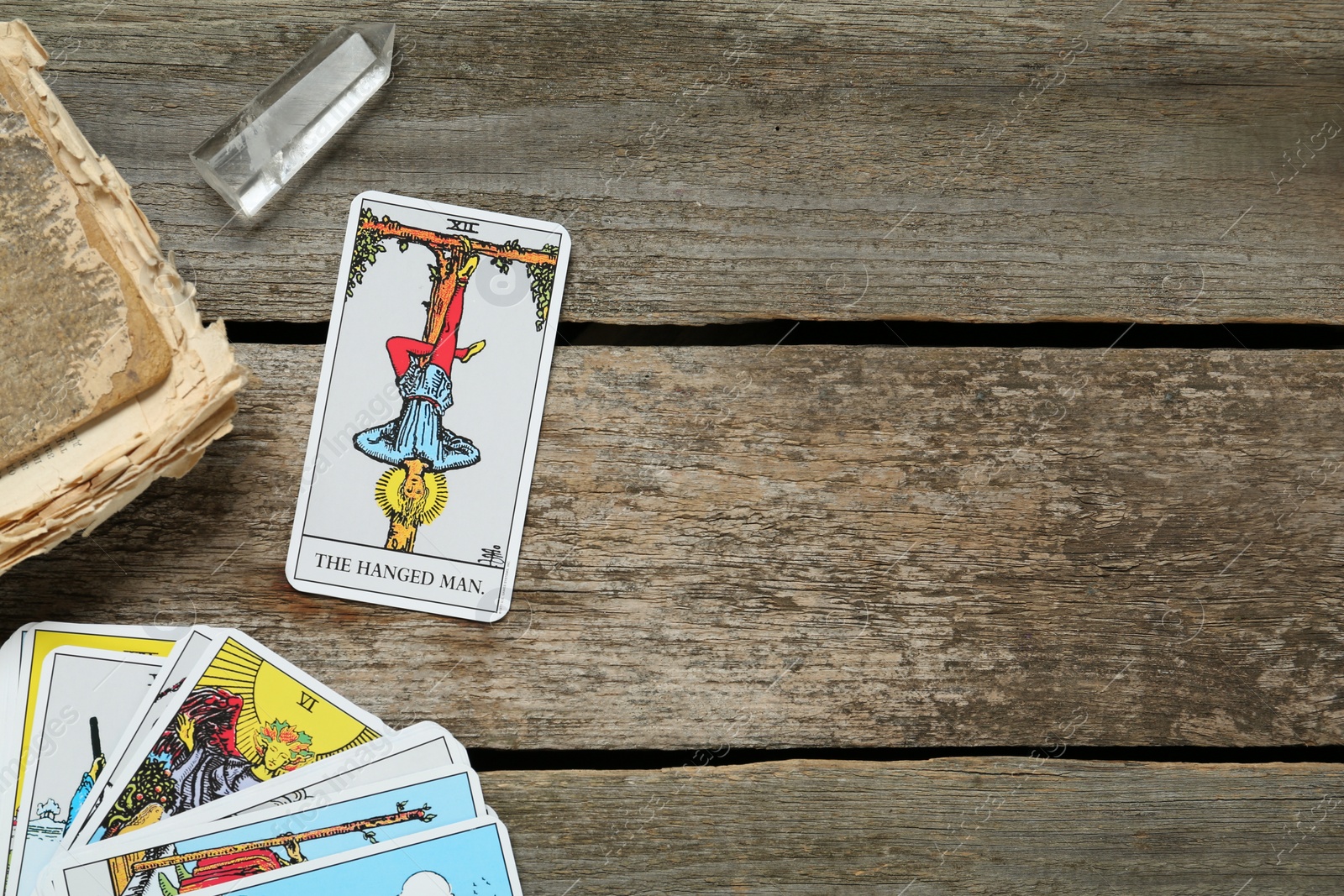 Photo of Hanged Man with other tarot cards, crystal and old book on wooden table, flat lay. Space for text