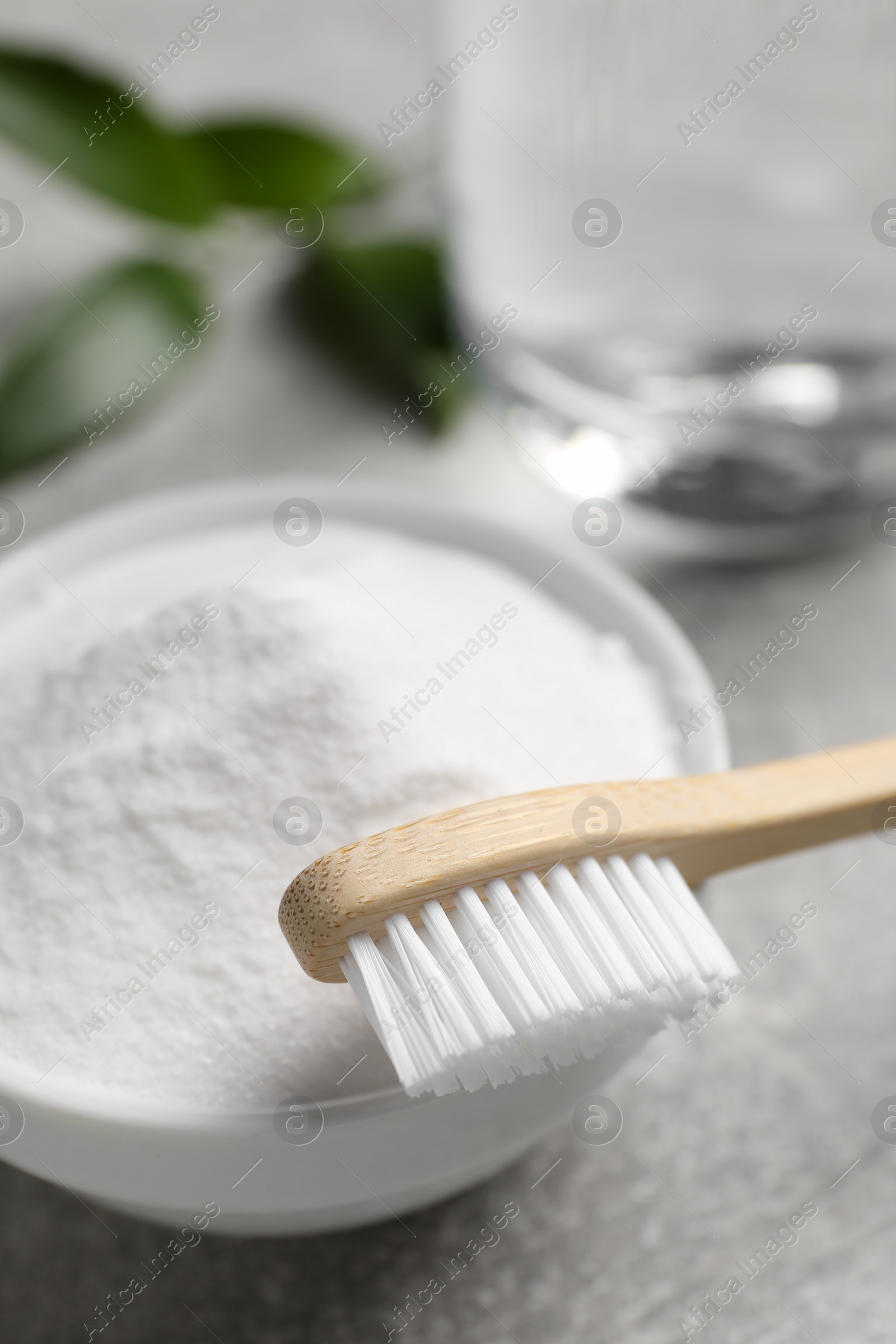 Photo of Bamboo toothbrush, green leaf and bowl of baking soda on grey table, closeup