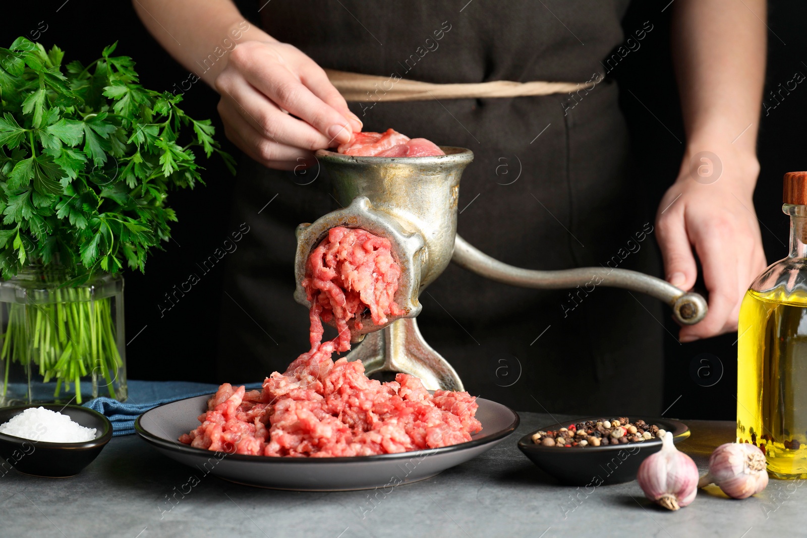 Photo of Woman making beef mince with manual meat grinder at grey table, closeup