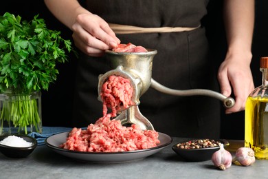 Photo of Woman making beef mince with manual meat grinder at grey table, closeup