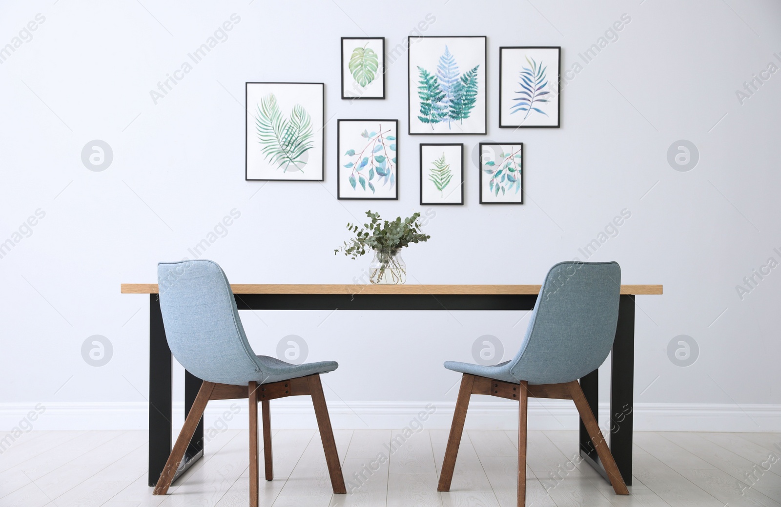 Photo of Stylish room interior with modern table, chairs and paintings of tropical leaves. Idea for design