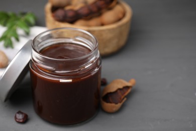 Photo of Jar of tasty tamarind sauce and fresh pods on grey wooden table. Space for text